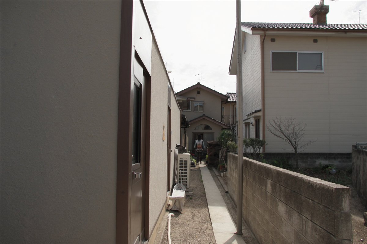 両側を建物に挟まれた細長い通路の奥に建つ住宅。旗竿地は不整形地補正や間口狭小補正の対象になる