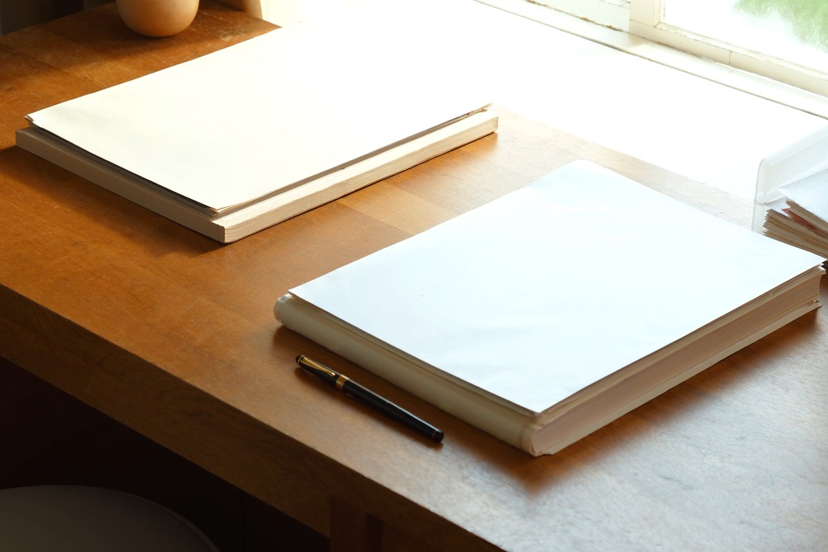 明るい窓辺の机に並べたノートと万年筆。エンディングノートと遺言書は役割が異なる